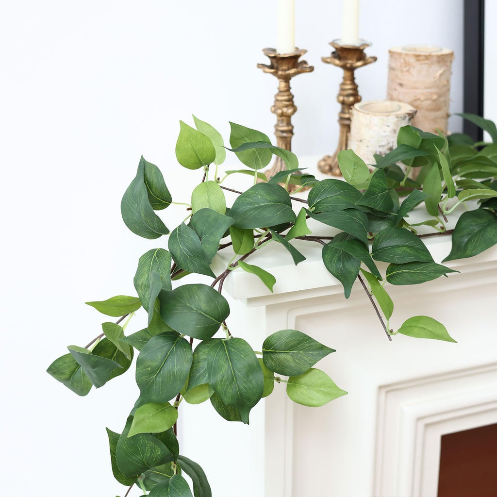 Artificial green vine garland with silk leaves draped over a white mantelpiece with decorative candle holders.