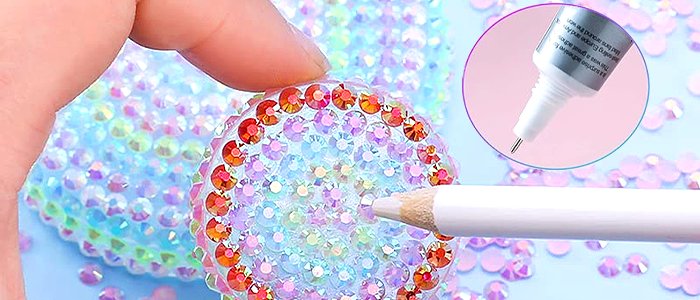 Close-up of a hand using a wax pencil to place rhinestones on a craft project, with an inset of a glue bottle.