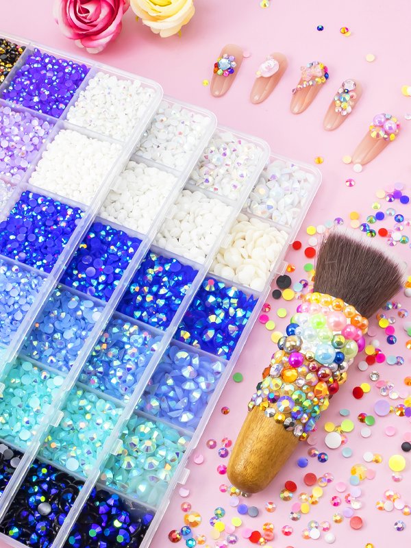 Assortment of colorful rhinestones in a divided case, with decorated nail tips and a craft brush on a pink background.