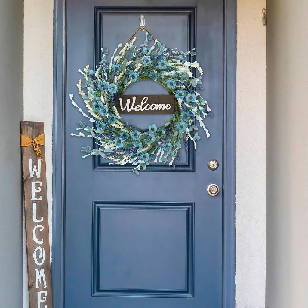 Blue forsythia wreath with white flowers and lavender accents hanging on a blue door with a wooden welcome sign