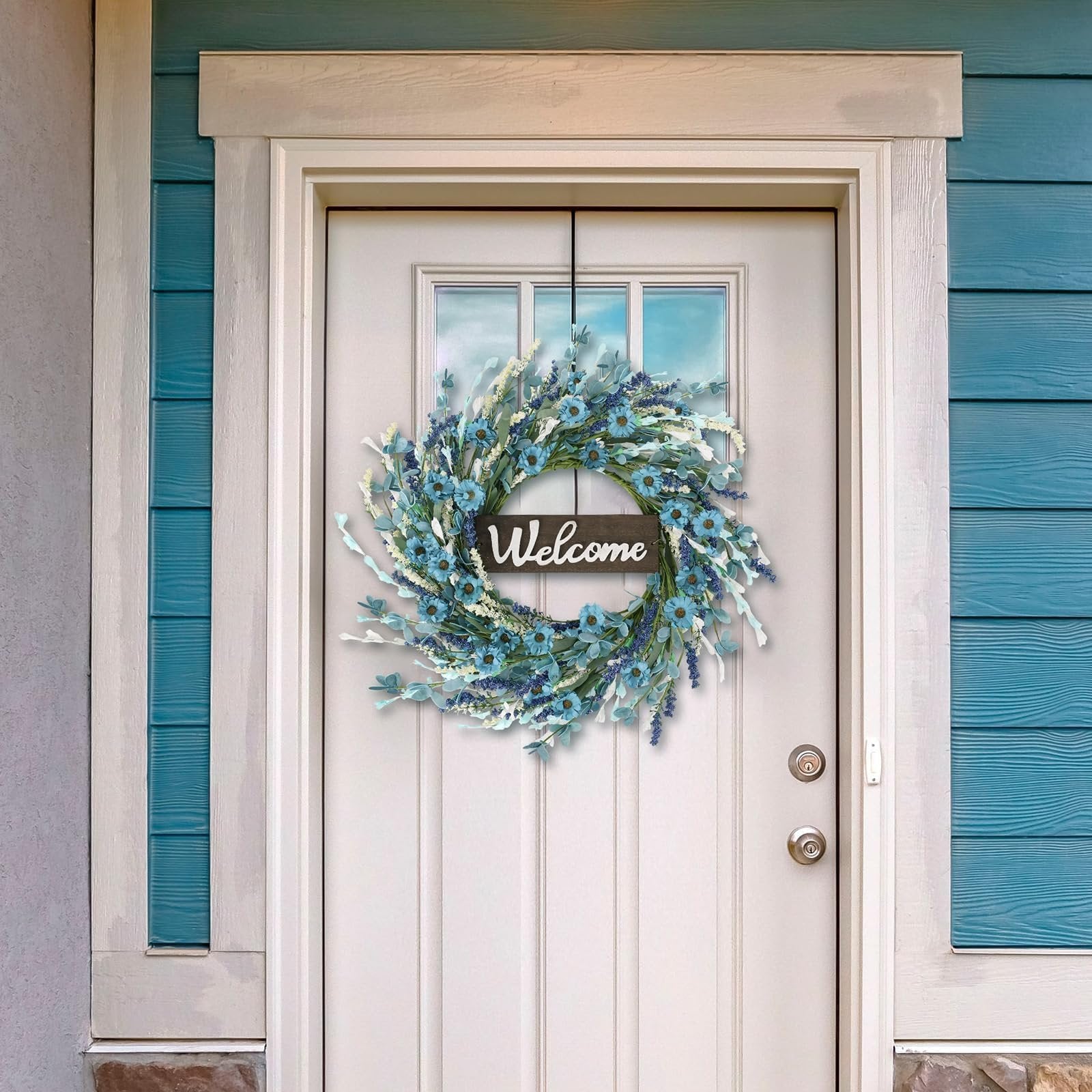 Blue forsythia and lavender wreath with a 'Welcome' sign hanging on a white door.