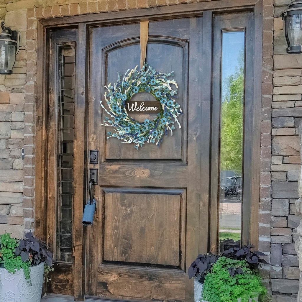 Blue forsythia wreath with 'Welcome' sign hanging on a wooden front door with stone accents.