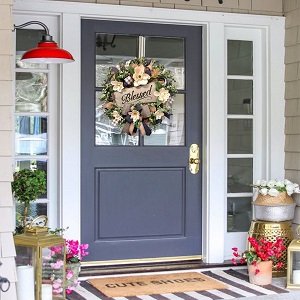 Front door decorated with a white magnolia wreath featuring a buffalo plaid bow and a 'Blessed' wooden plaque.