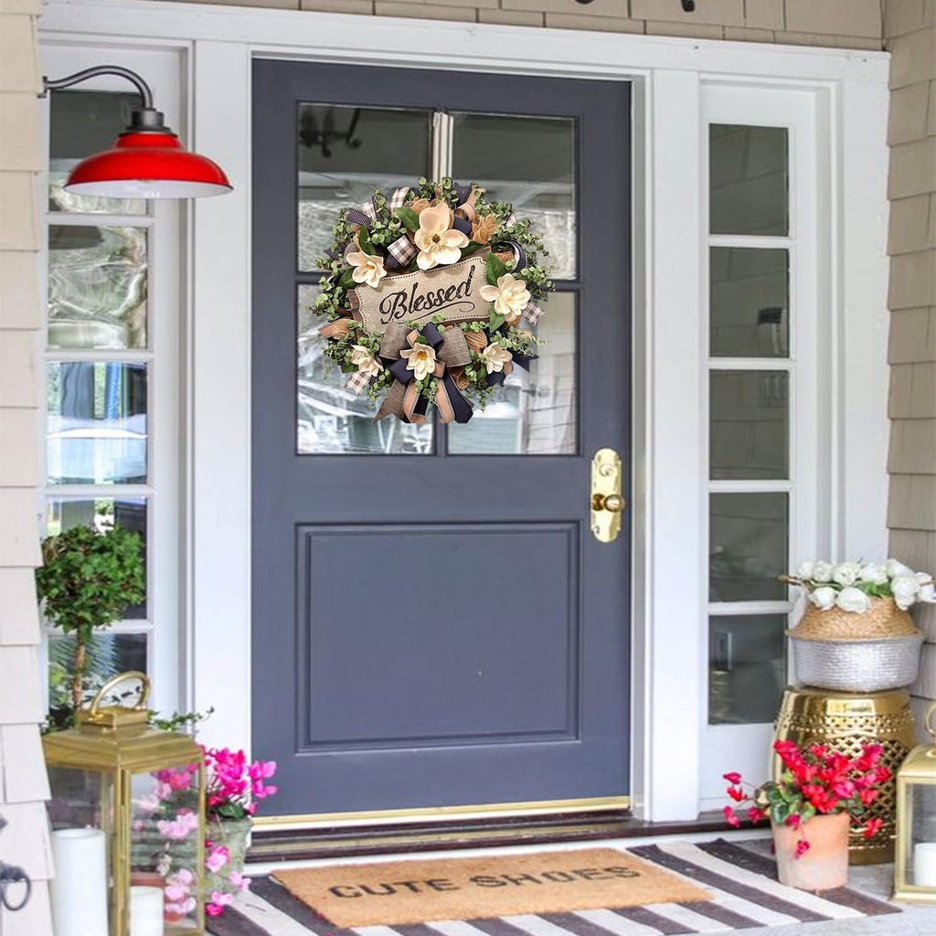 Magnolia wreath with buffalo plaid bow and 'Blessed' sign hanging on a dark blue front door.