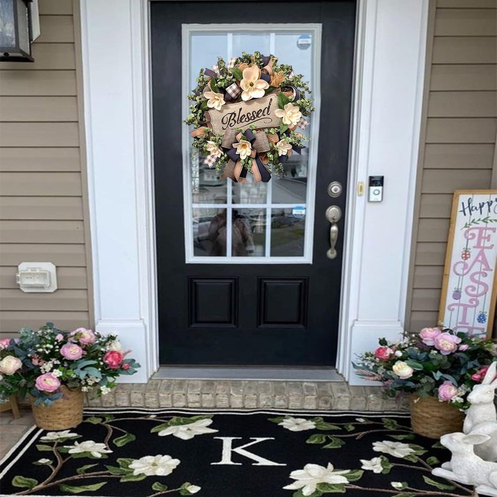 Magnolia wreath with 'Blessed' plaque and buffalo plaid bow hanging on a black front door.