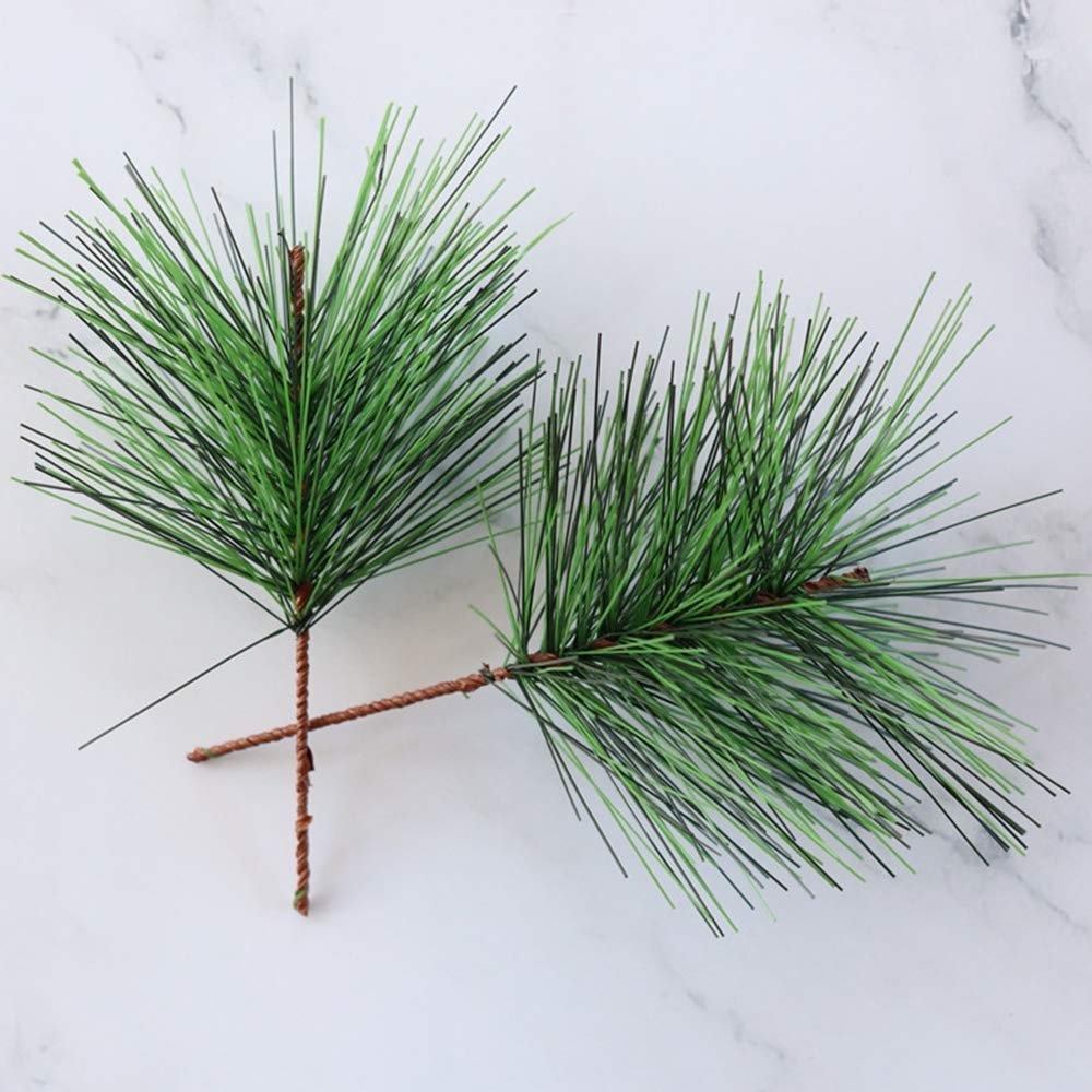 Two artificial green pine needle stems with brown wire stems on a white marble background.