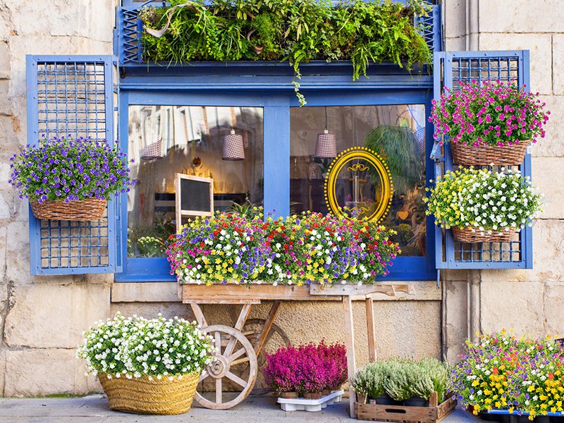 Assortment of artificial flowers in baskets and wooden crates displayed outside a blue window.