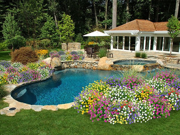 Lush garden landscaping with a swimming pool, hot tub, patio, and colorful flowers.