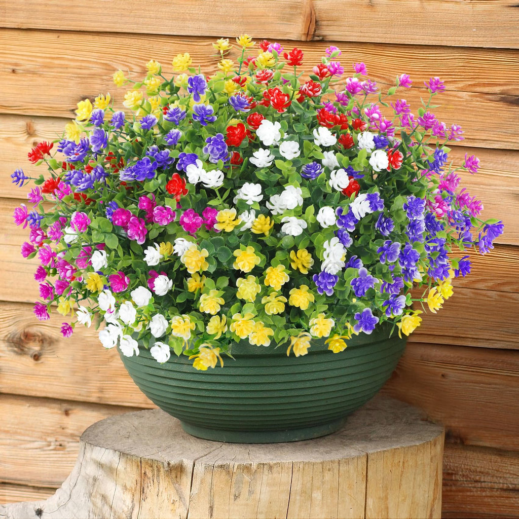 Artificial flowers in a green planter on a wooden stump against a wooden wall, featuring red, purple, white, yellow, and magenta blooms.