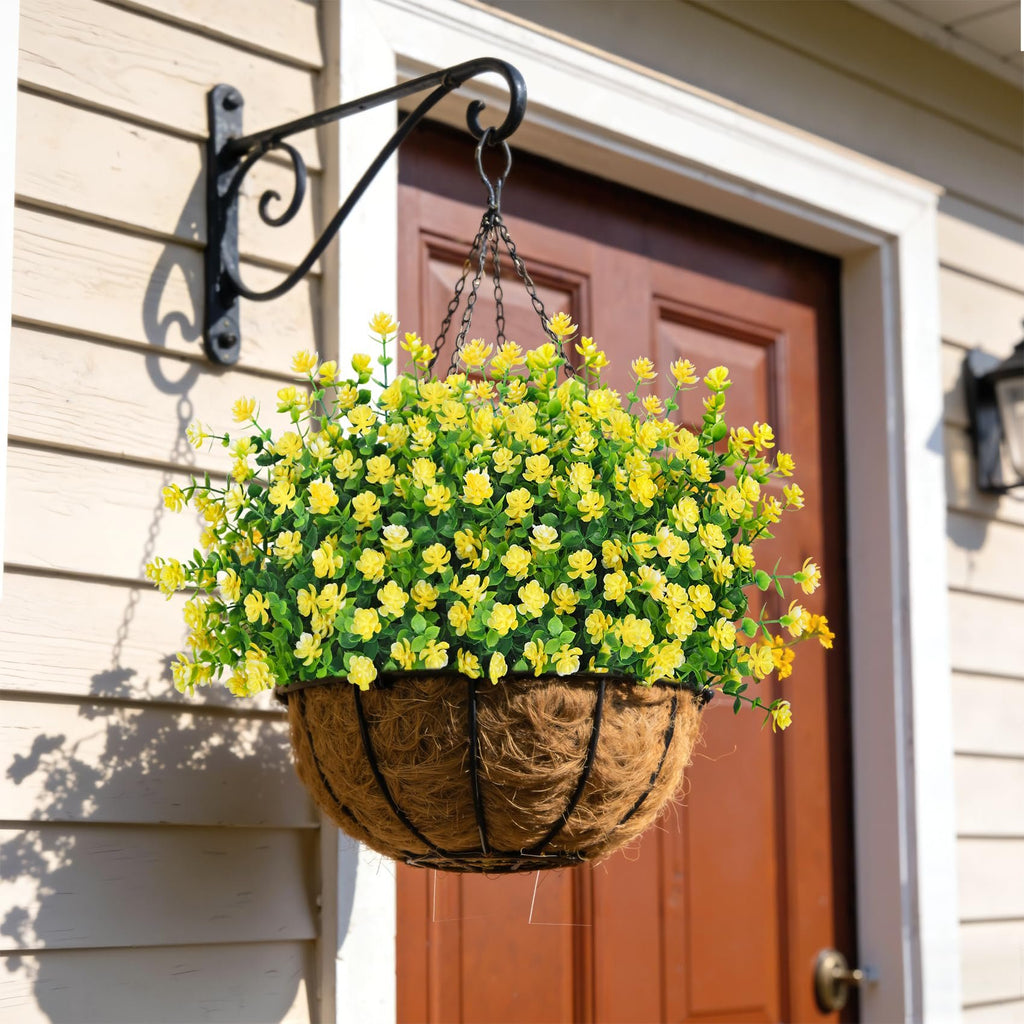 Hanging basket filled with yellow artificial flowers, suspended from a bracket on a house exterior.
