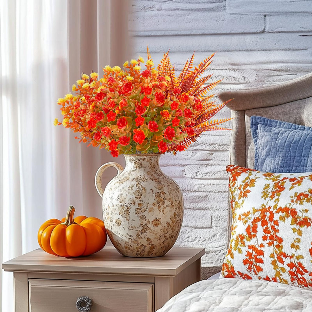 Artificial fall flower arrangement in a vase with a pumpkin on a nightstand next to a bed.