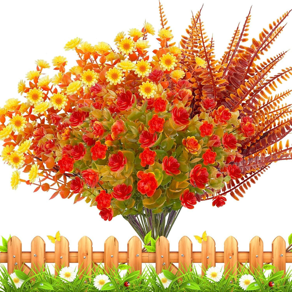 Artificial fall flowers bouquet with red roses, yellow daisies, and ferns, arranged above a wooden fence with grass and butterflies.