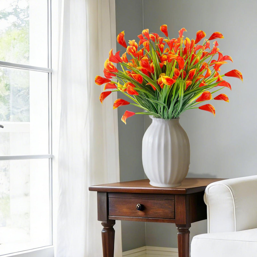 Bouquet of orange and yellow artificial calla lilies in a white vase on a wooden side table.