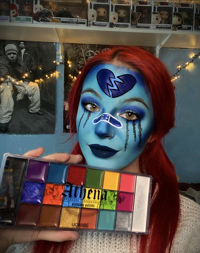 Woman with blue face paint and broken heart design holding a 20-color oil-based painting palette