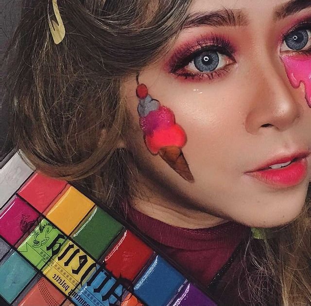 Woman with colorful ice cream cone face paint and makeup holding a palette of face paints.