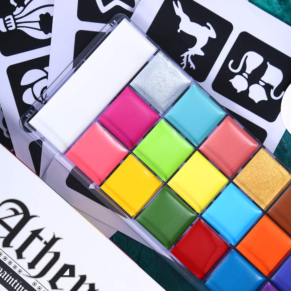 Close-up of a 20-color oil-based face and body paint palette with various vibrant colors, including metallic silver and gold, arranged in a grid. Tattoo stencils are visible in the background.
