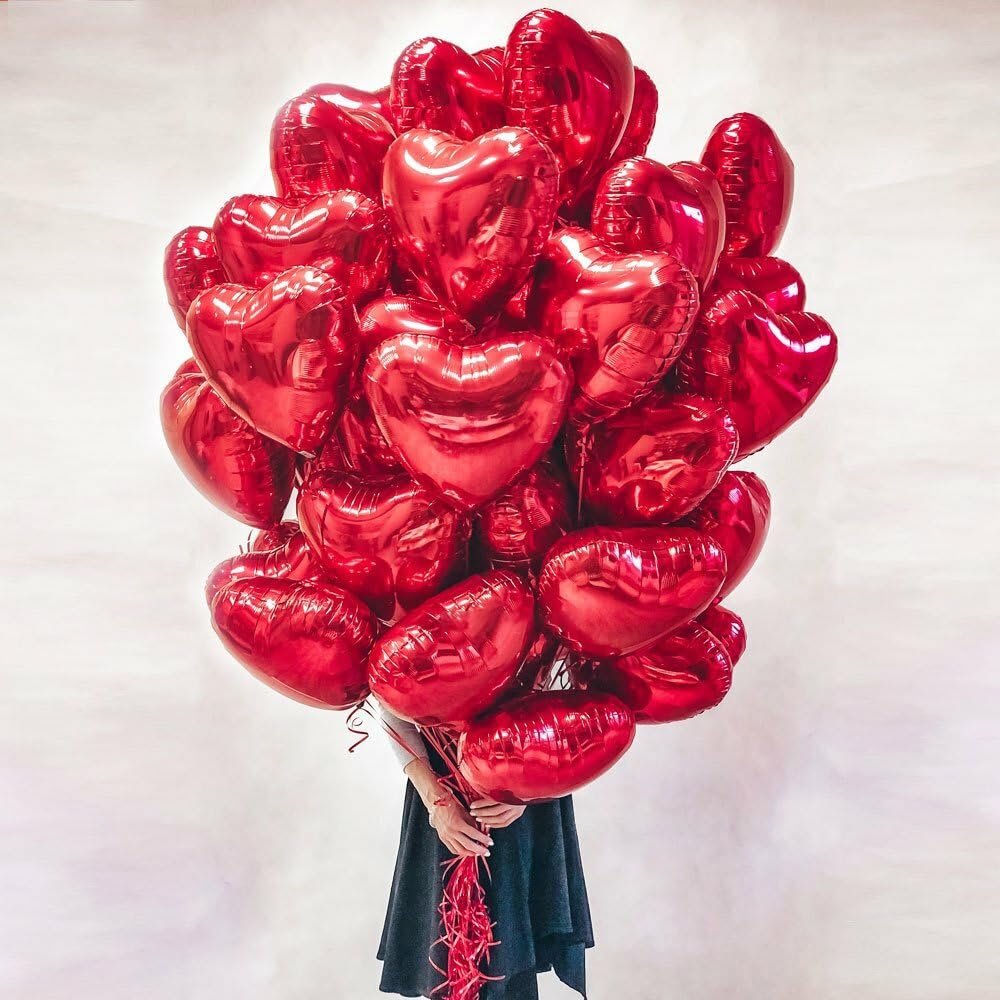 A large bouquet of red heart-shaped foil balloons held by a person wearing a dark skirt against a white background.