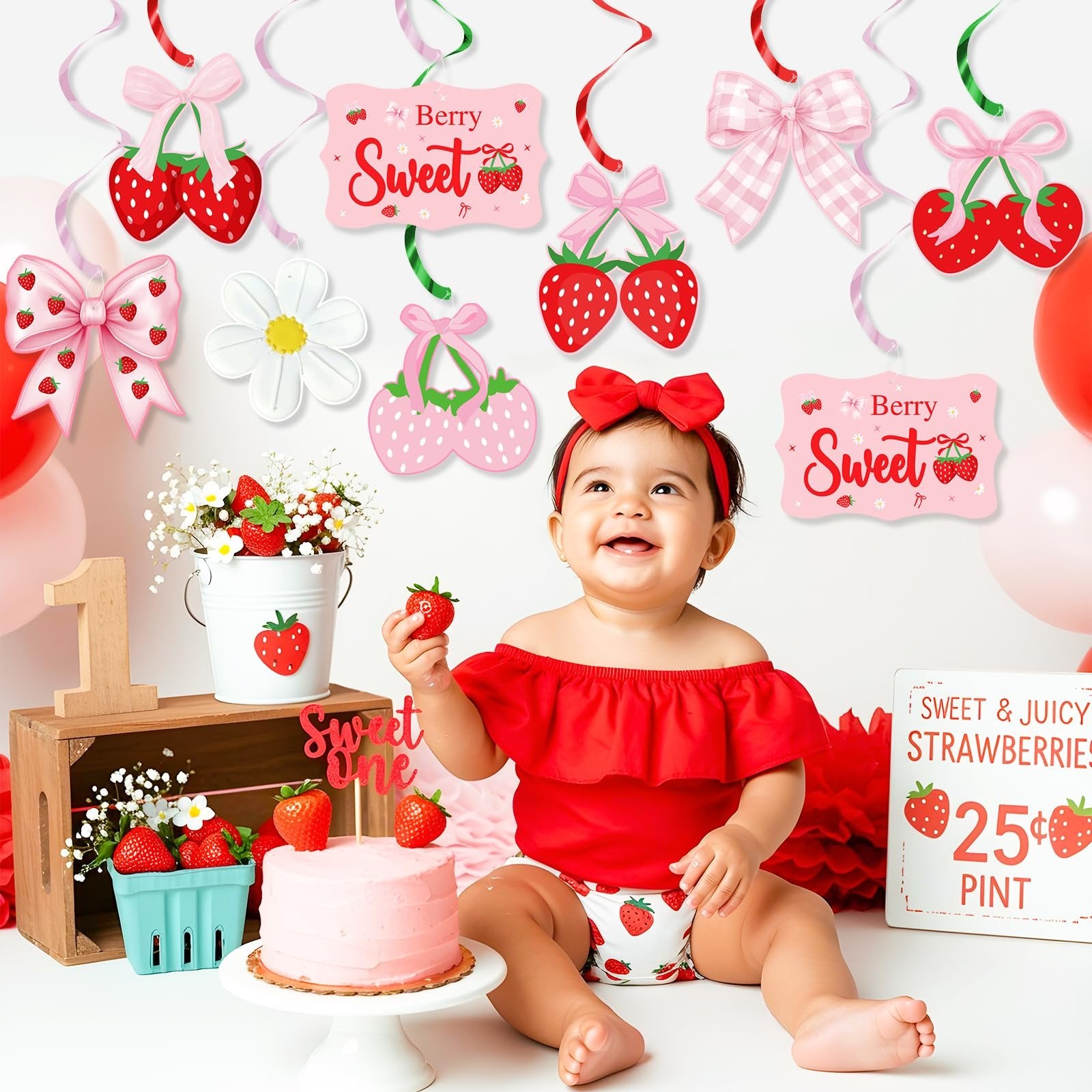 Baby in red outfit celebrating first birthday with strawberry-themed decorations and cake