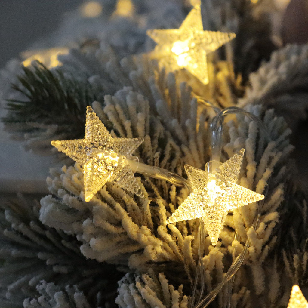 Close-up of warm white star-shaped LED string lights on a flocked pine branch.