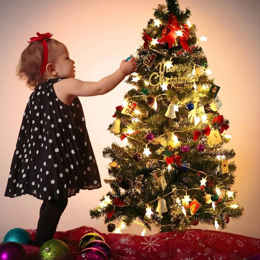 Toddler decorating a Christmas tree with warm white star string lights and ornaments.