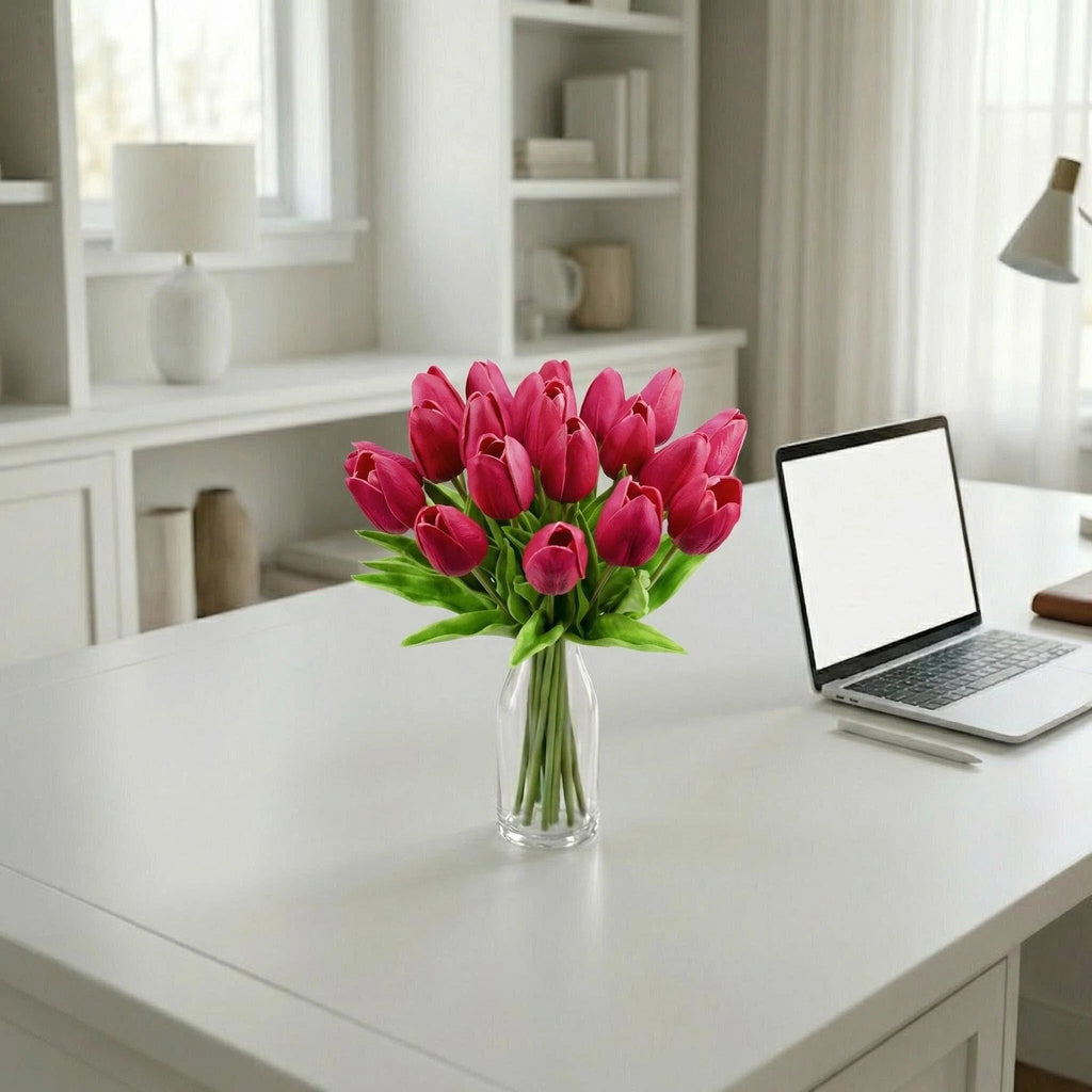 Bouquet of 20 hot pink artificial tulips in a clear vase on a white desk next to a laptop.