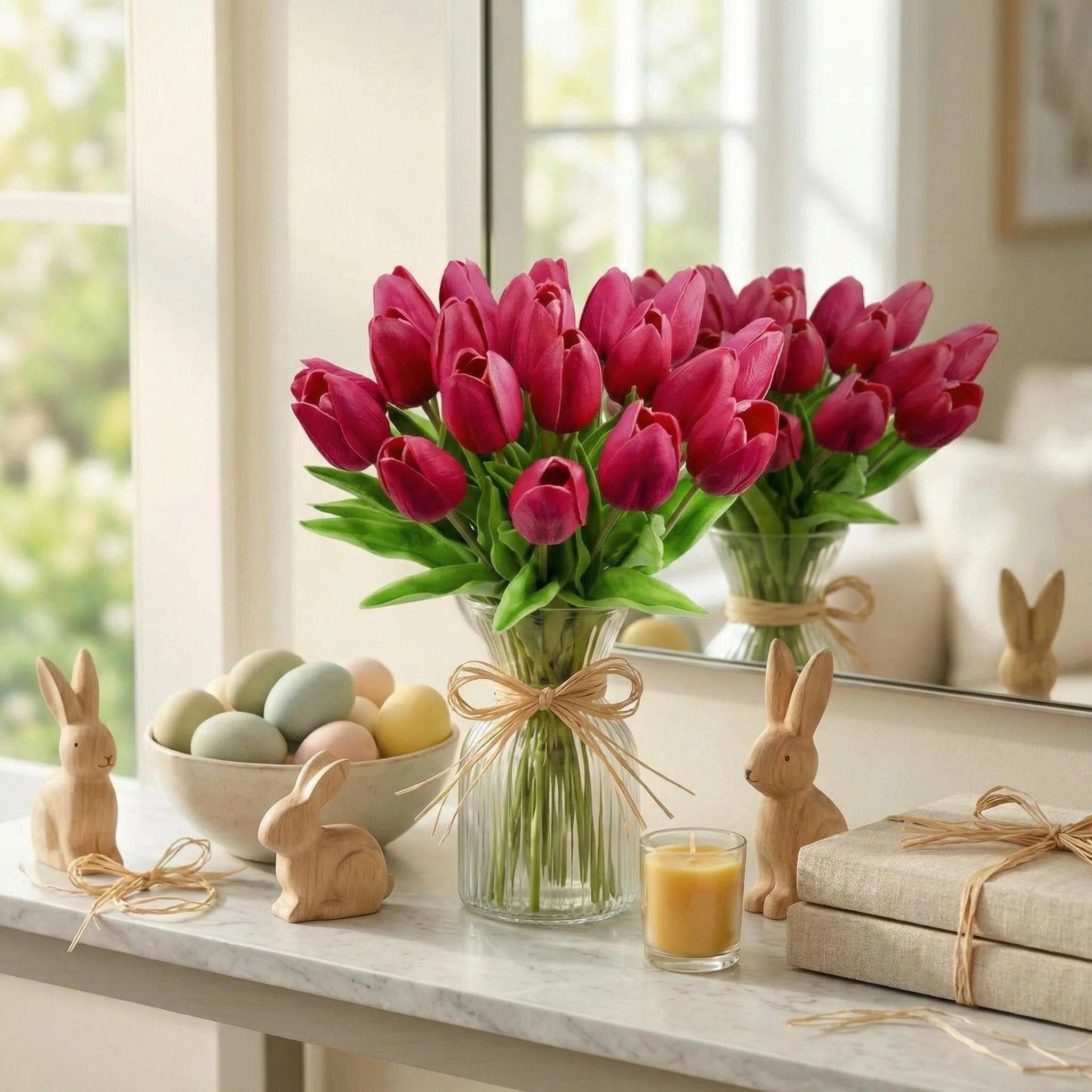 A vase of hot pink artificial tulips sits on a marble surface with Easter decor, including wooden bunnies and pastel eggs.