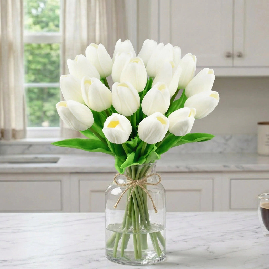 A bouquet of 20 white artificial tulips in a glass vase on a marble countertop, with kitchen cabinets and a window in the background.