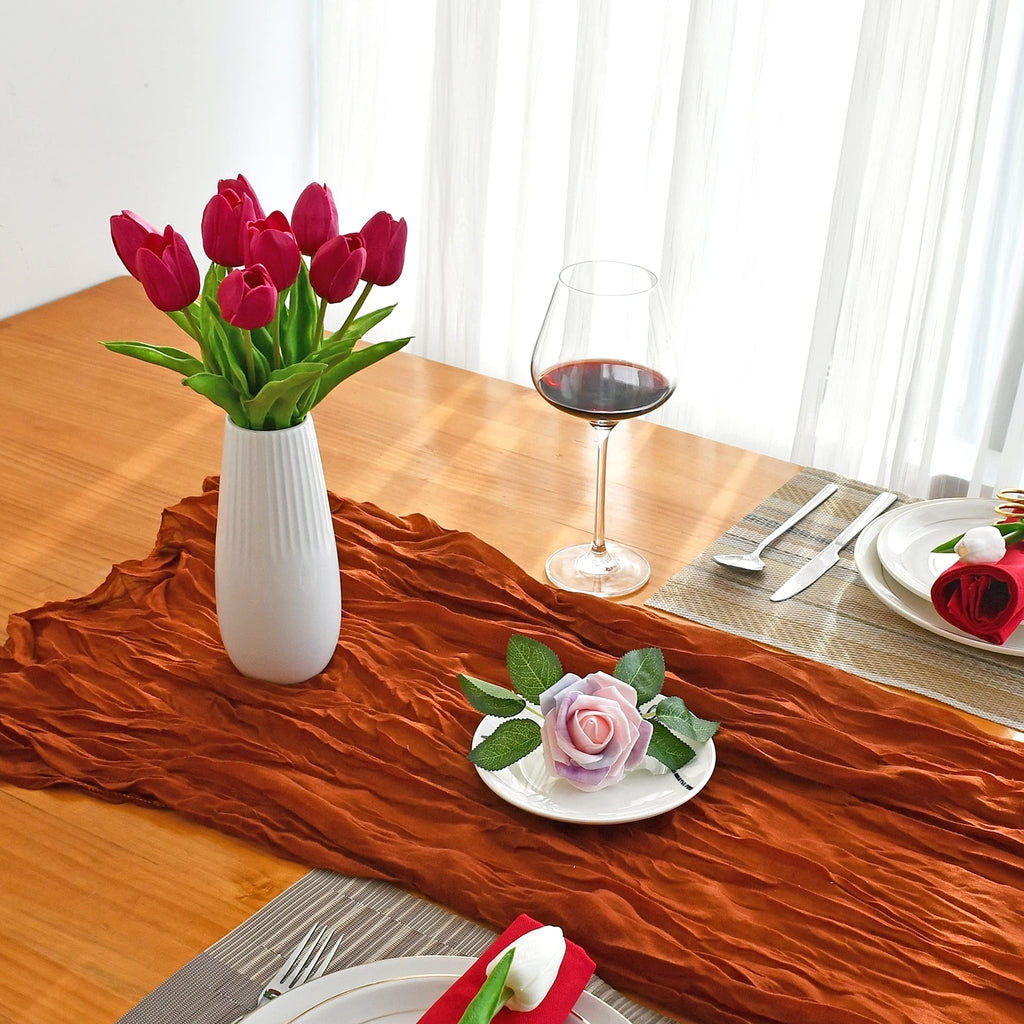 Table setting with a vase of hot pink artificial tulips, a glass of red wine, and place settings on a wooden table.