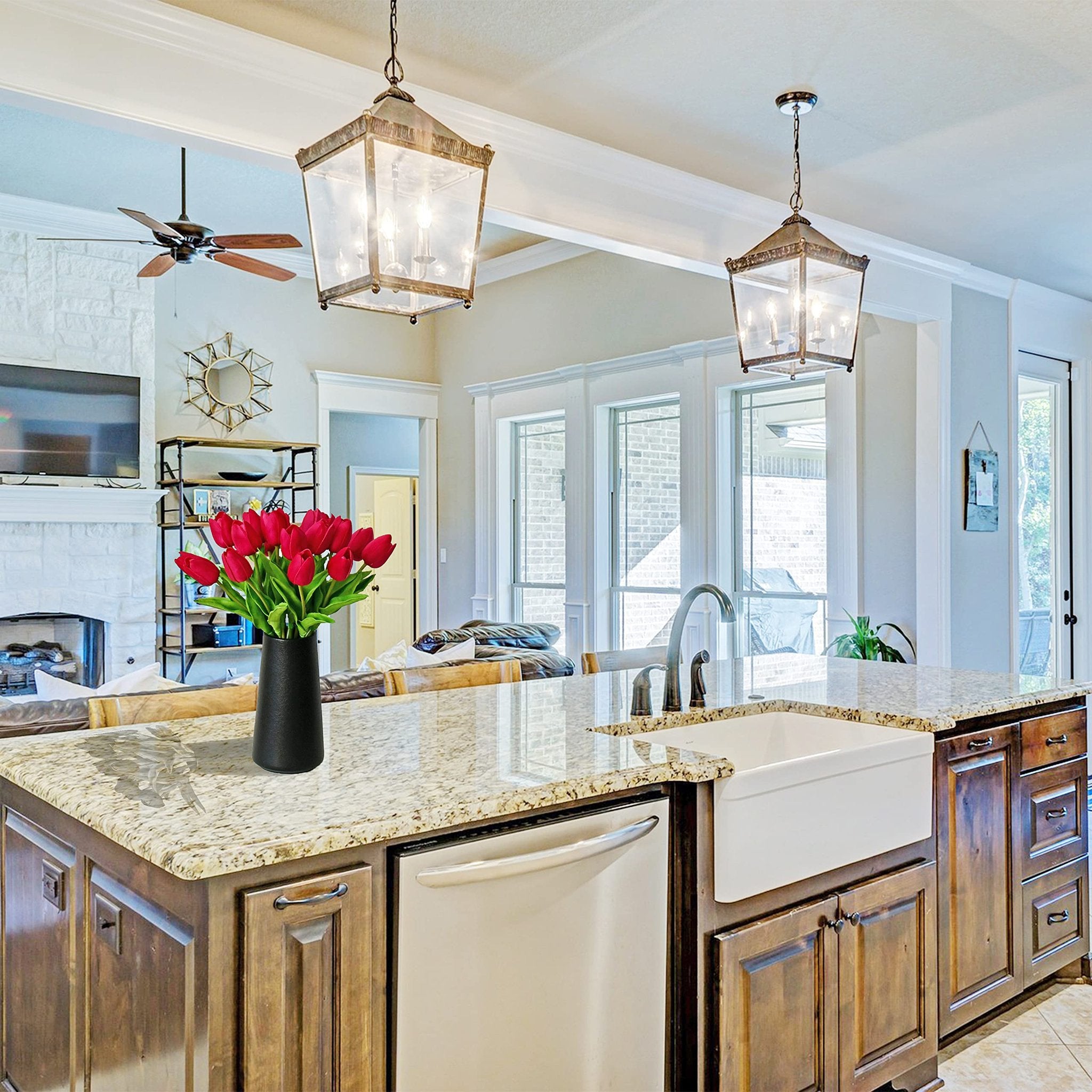 A vase of hot pink artificial tulips sits on a granite kitchen island in front of a sink and faucet.