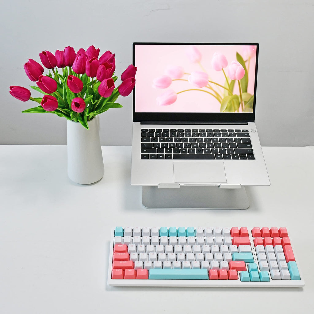 A vase of hot pink artificial tulips sits next to a laptop displaying pink tulips, with a colorful keyboard in the foreground.