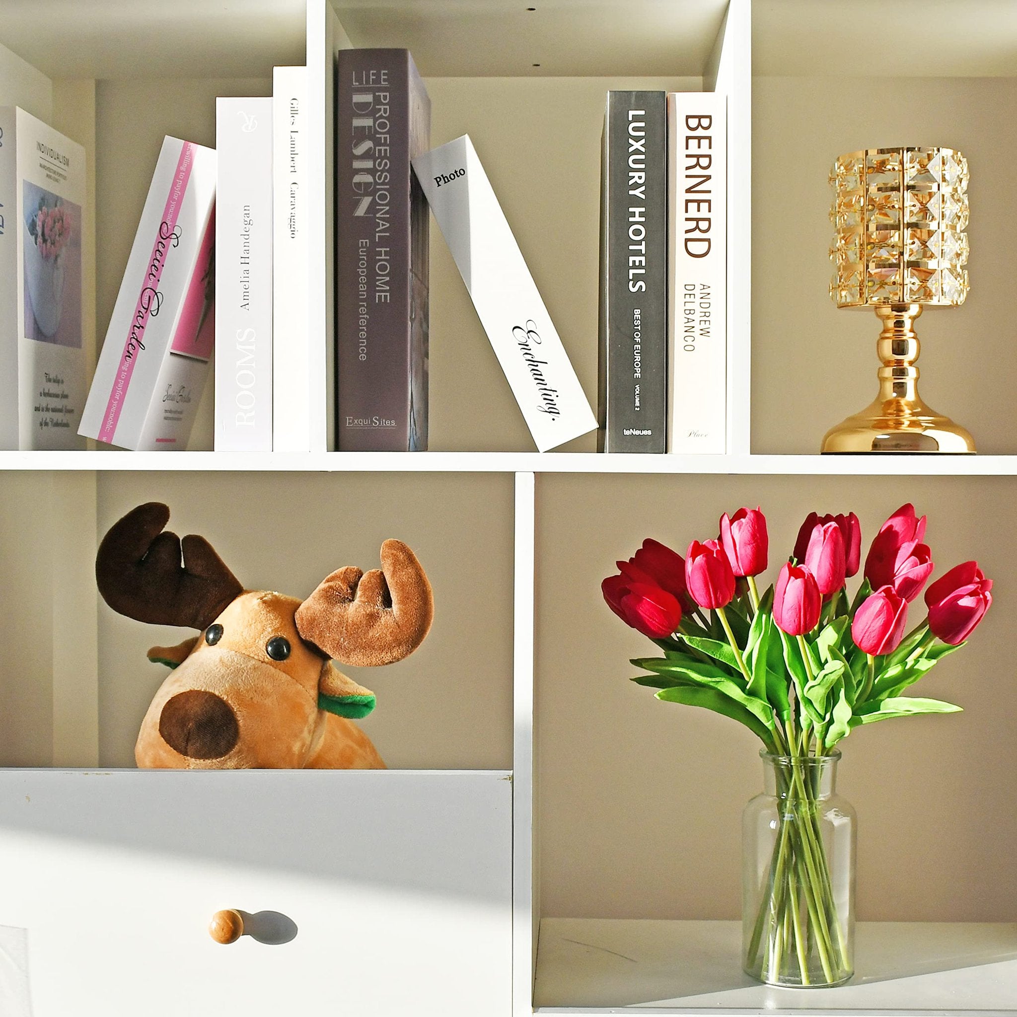 A shelf with books, a decorative lamp, a stuffed moose, and a vase of red tulips.