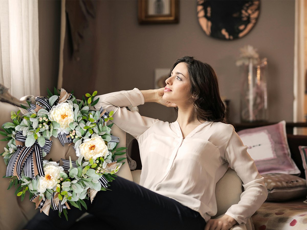 Artificial lamb's ear wreath with white peonies and berries, displayed next to a woman relaxing on a couch.