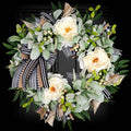 Artificial lamb's ear wreath with white peonies, berries, and buffalo plaid bow against a black background.