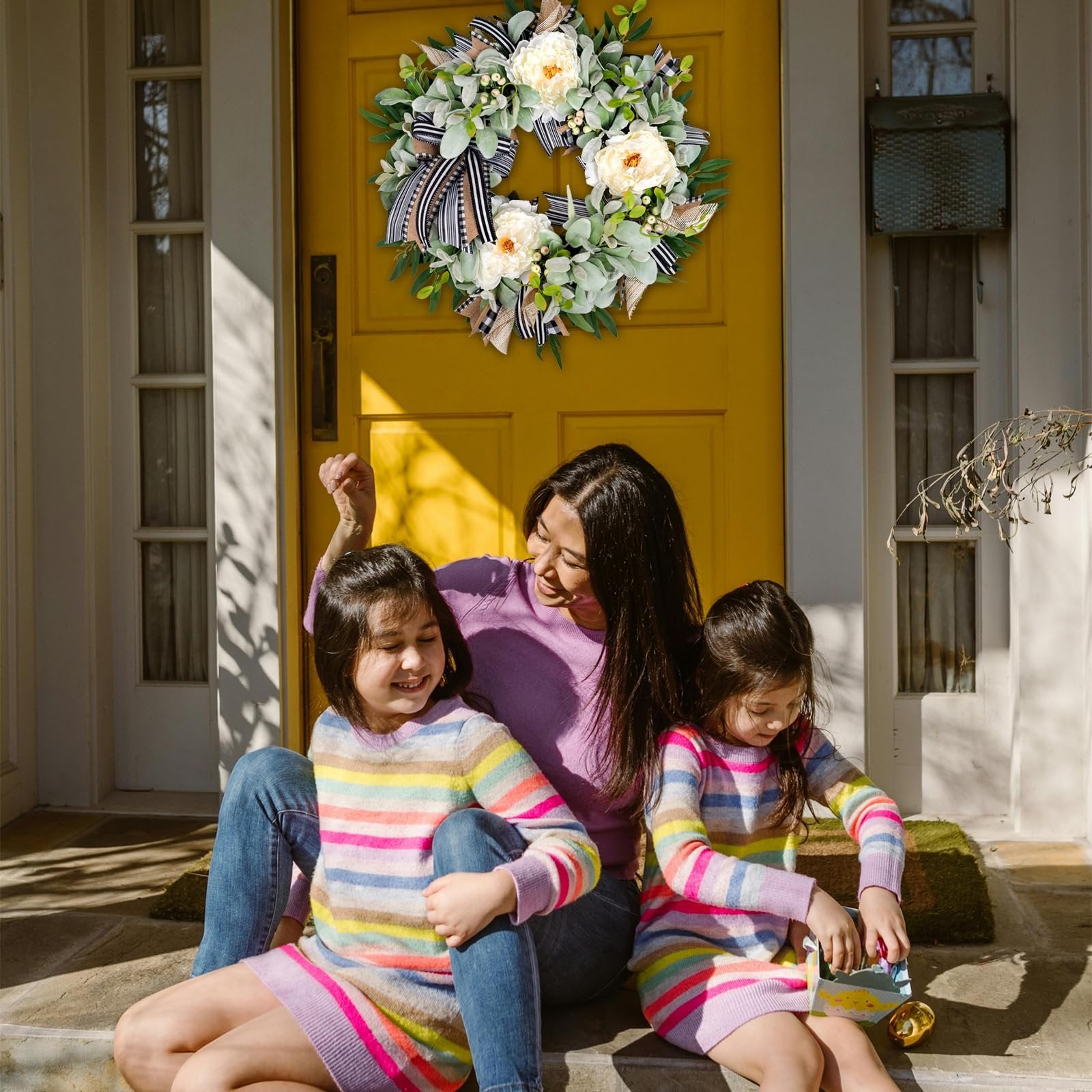 Mother and two daughters sitting on porch steps with a wreath on the door behind them.