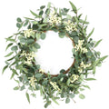 Eucalyptus wreath with white berries on a white background, showing multiple leaf types and a woven base.