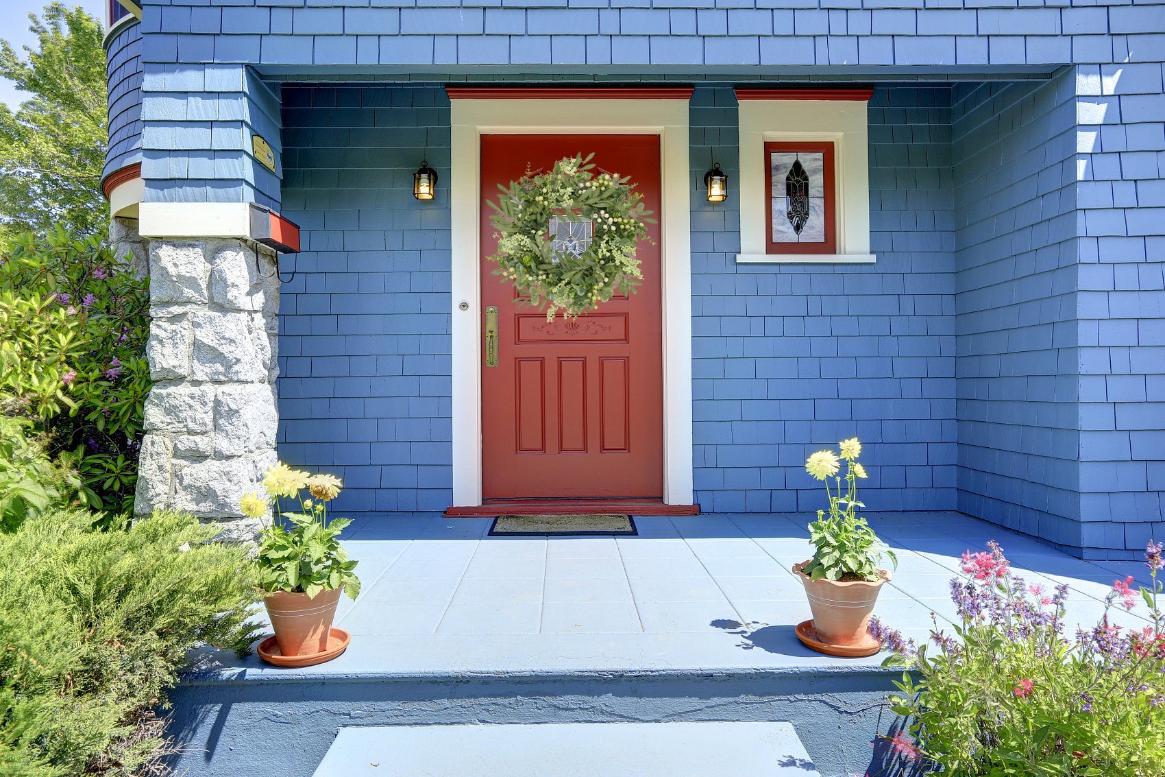 Eucalyptus wreath with olive leaves and berries hanging on a red front door of a blue house.