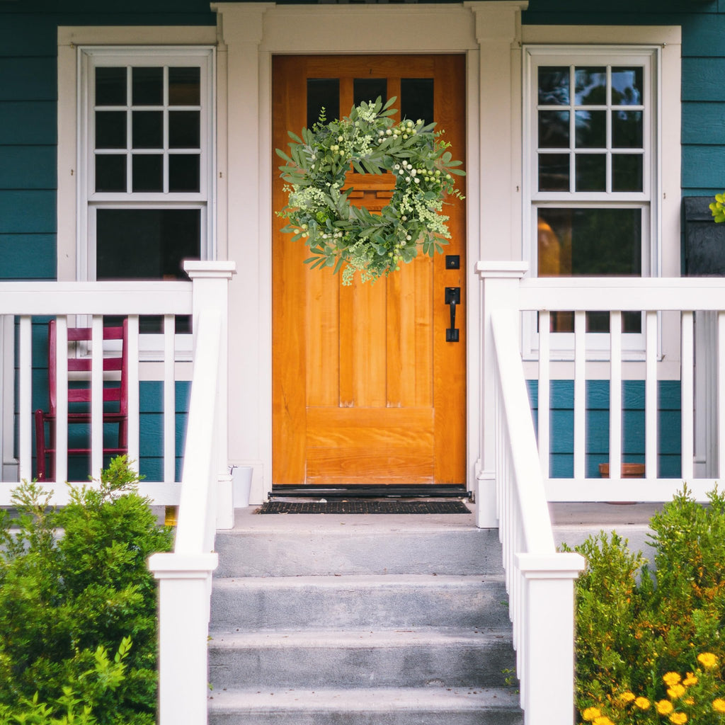Eucalyptus and berry wreath hanging on a wooden front door with a porch and steps.