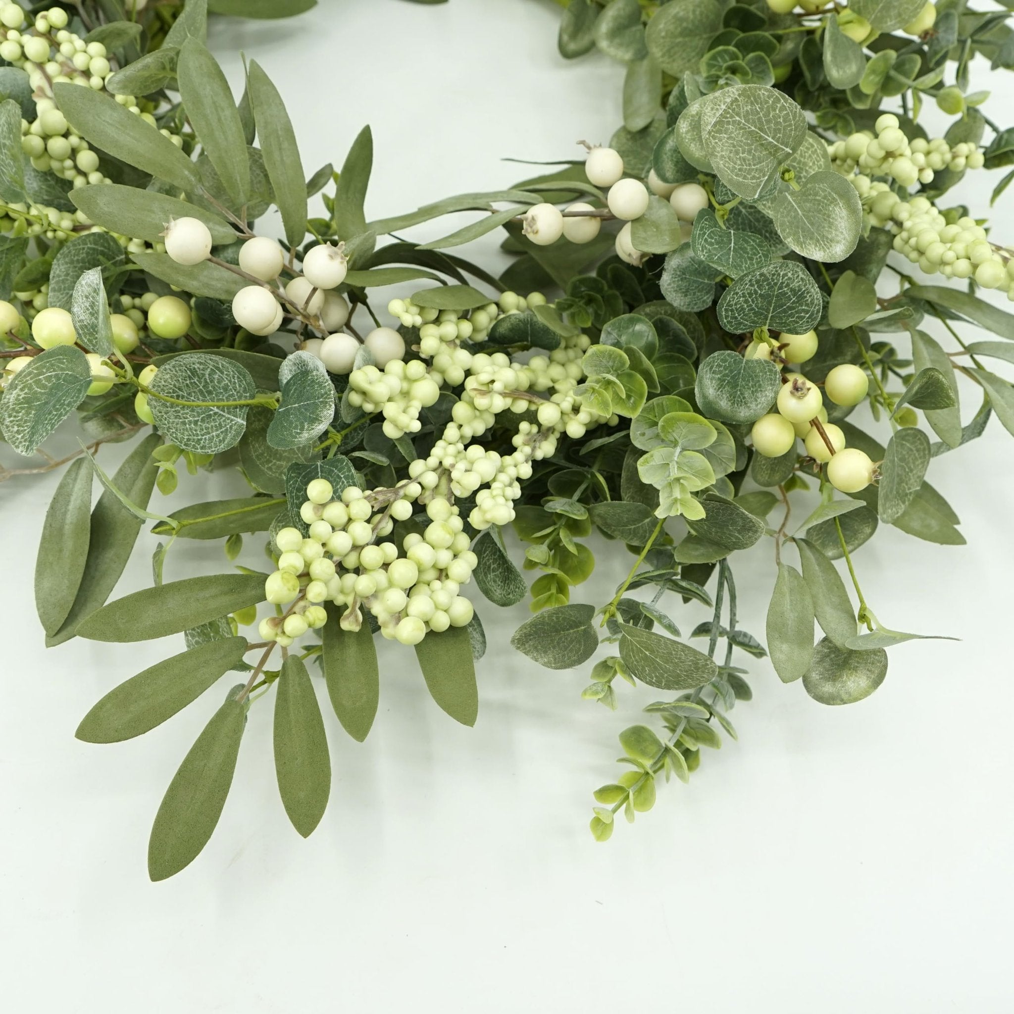 Close-up of a 20-inch artificial wreath with eucalyptus leaves, olive leaves, and white berries on a white background.