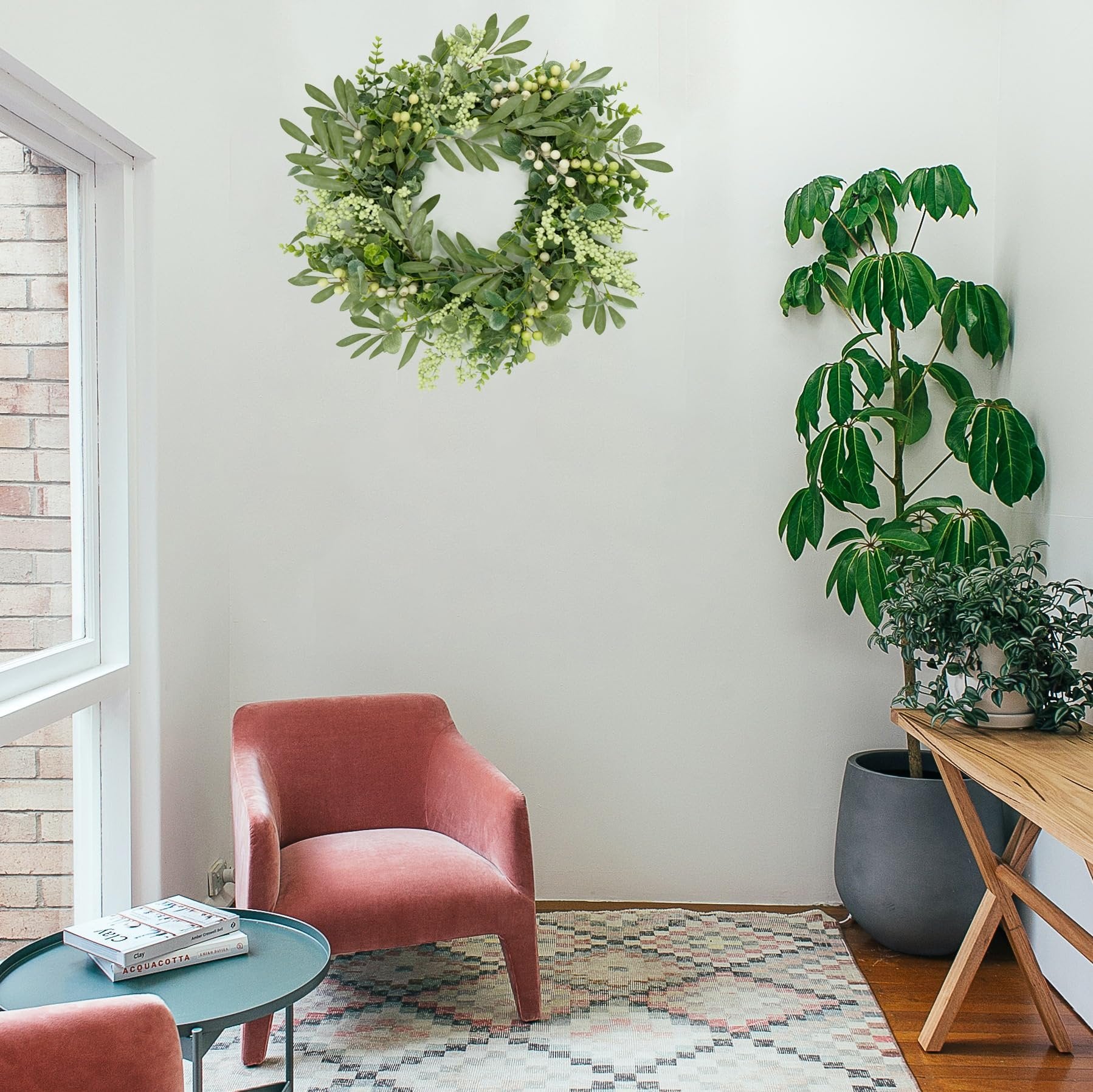 Eucalyptus and olive leaf wreath with white berries hanging on a wall above a pink armchair.