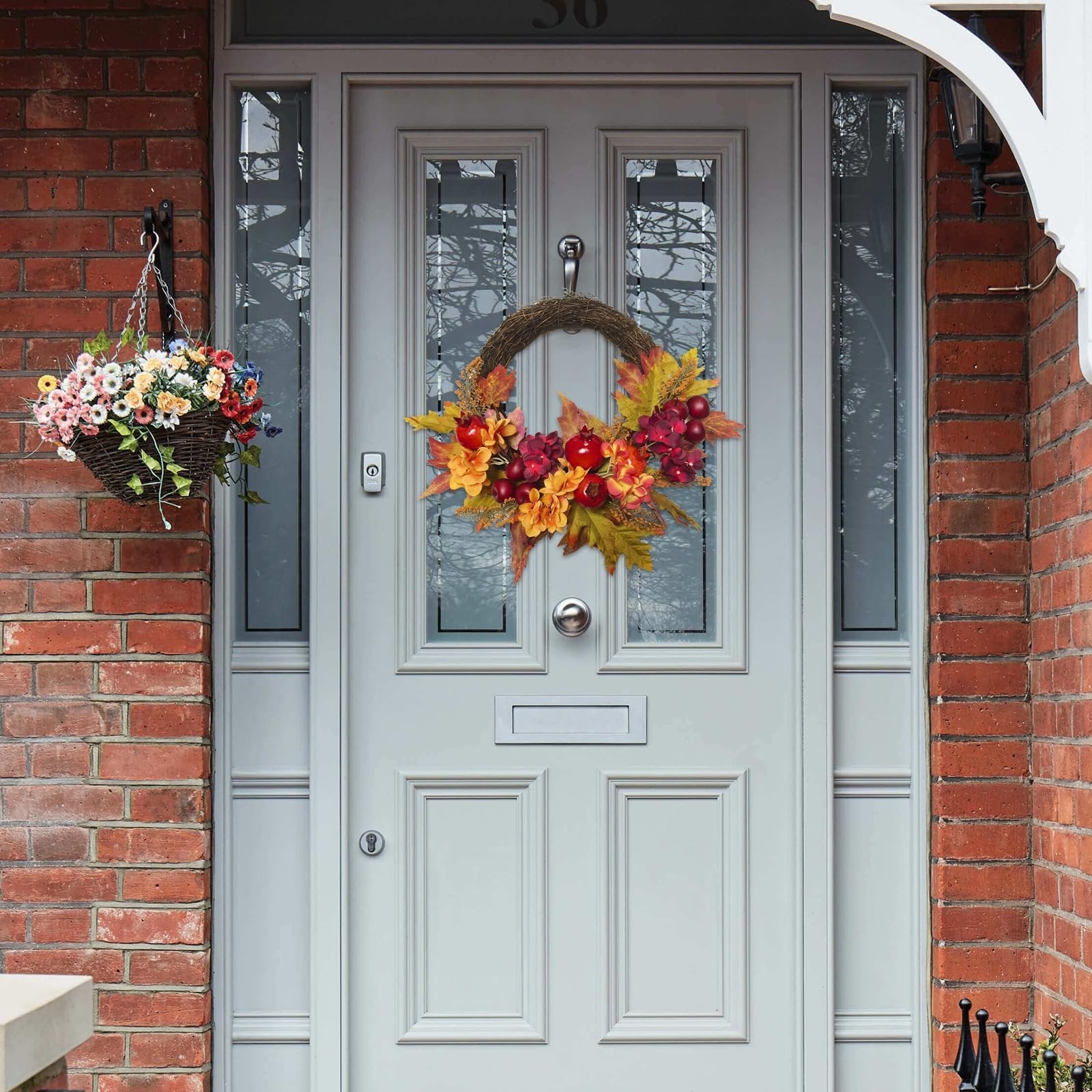 Front door decorated with a fall wreath featuring apples, pomegranates, and maple leaves, with a hanging flower basket to the left.