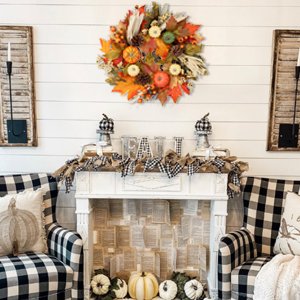 Fall wreath with pumpkins, maple leaves, berries, pine cones, and corn silk hanging above a fireplace decorated for autumn.