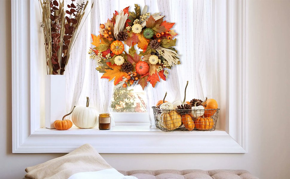 Fall wreath with pumpkins, maple leaves, berries, pine cones, and corn silk hanging on a window with sheer curtains.