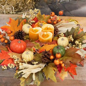 Fall wreath arrangement with pumpkins, maple leaves, berries, pine cones, and lit candles on a wooden surface.