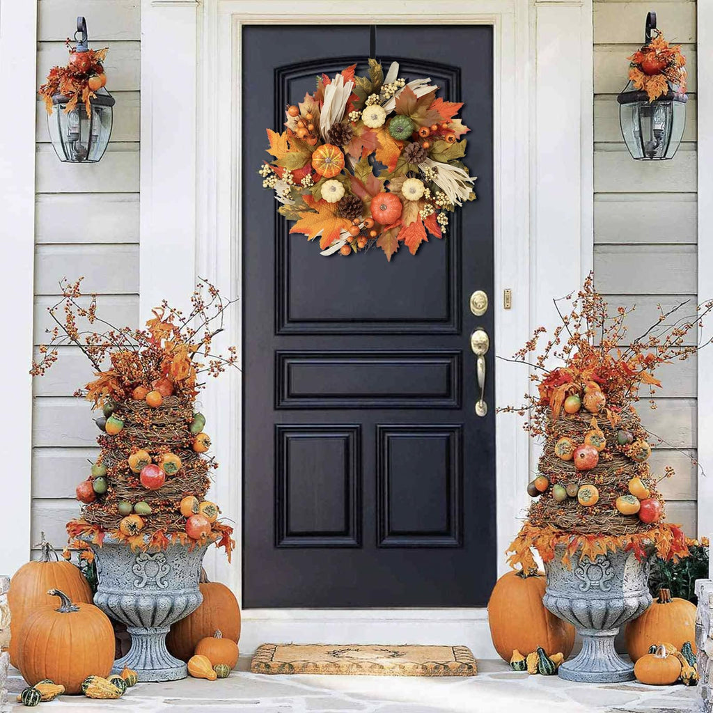 Fall wreath with pumpkins, maple leaves, berries, pine cones, and corn silk hanging on a black door, flanked by decorative urns and pumpkins.