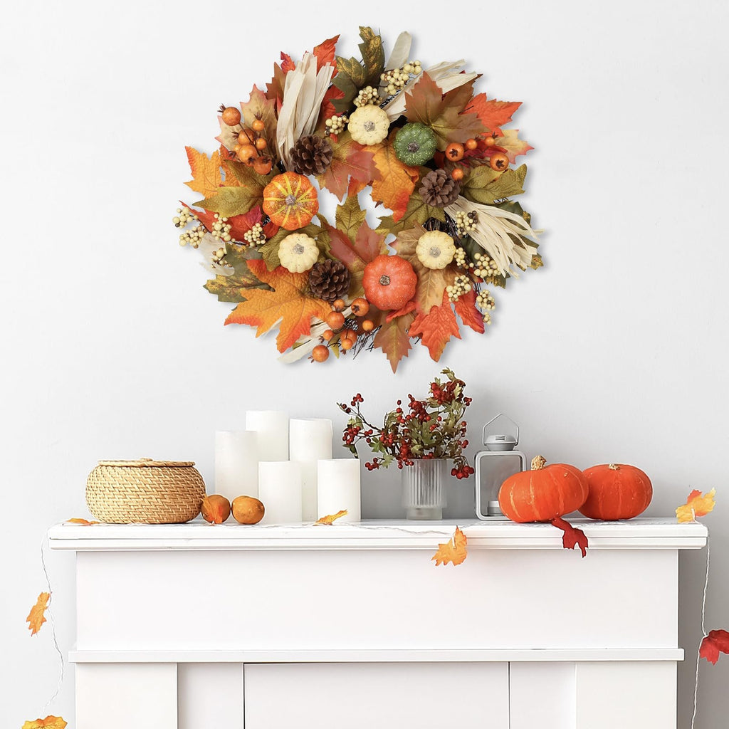 Fall wreath with pumpkins, maple leaves, pine cones, and berries hanging on a white wall above a mantelpiece.