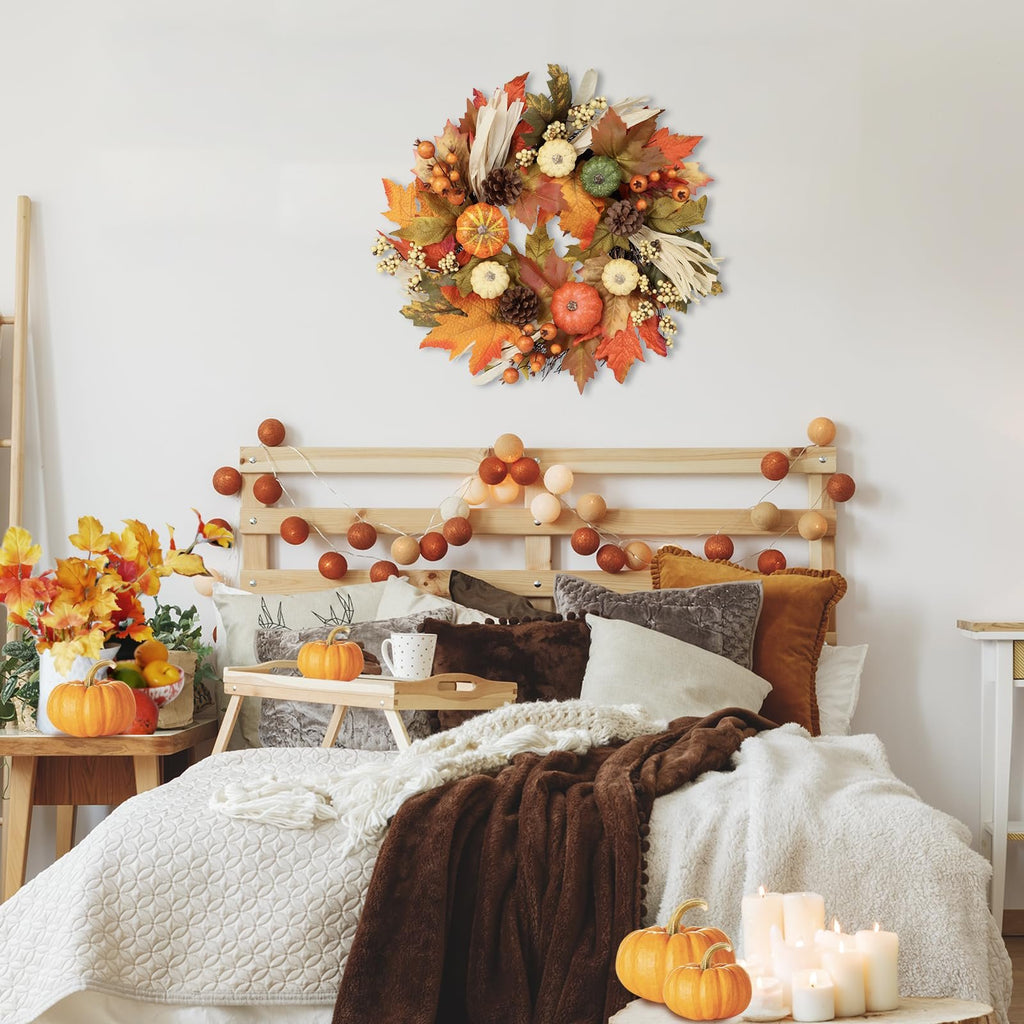 Fall wreath with pumpkins, maple leaves, berries, pine cones, and corn silk hanging above a bed decorated for autumn.