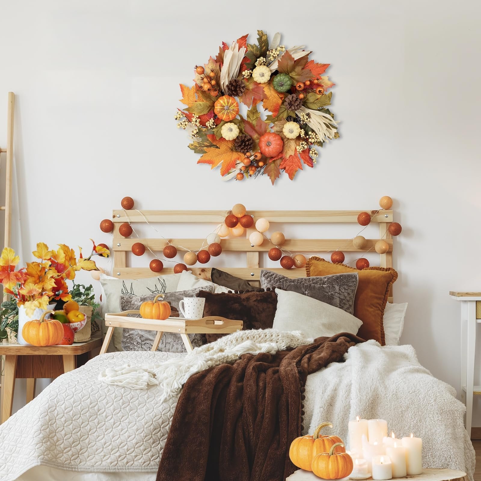 Fall wreath with pumpkins, maple leaves, berries, pine cones, and corn silk hanging above a bed decorated for autumn.