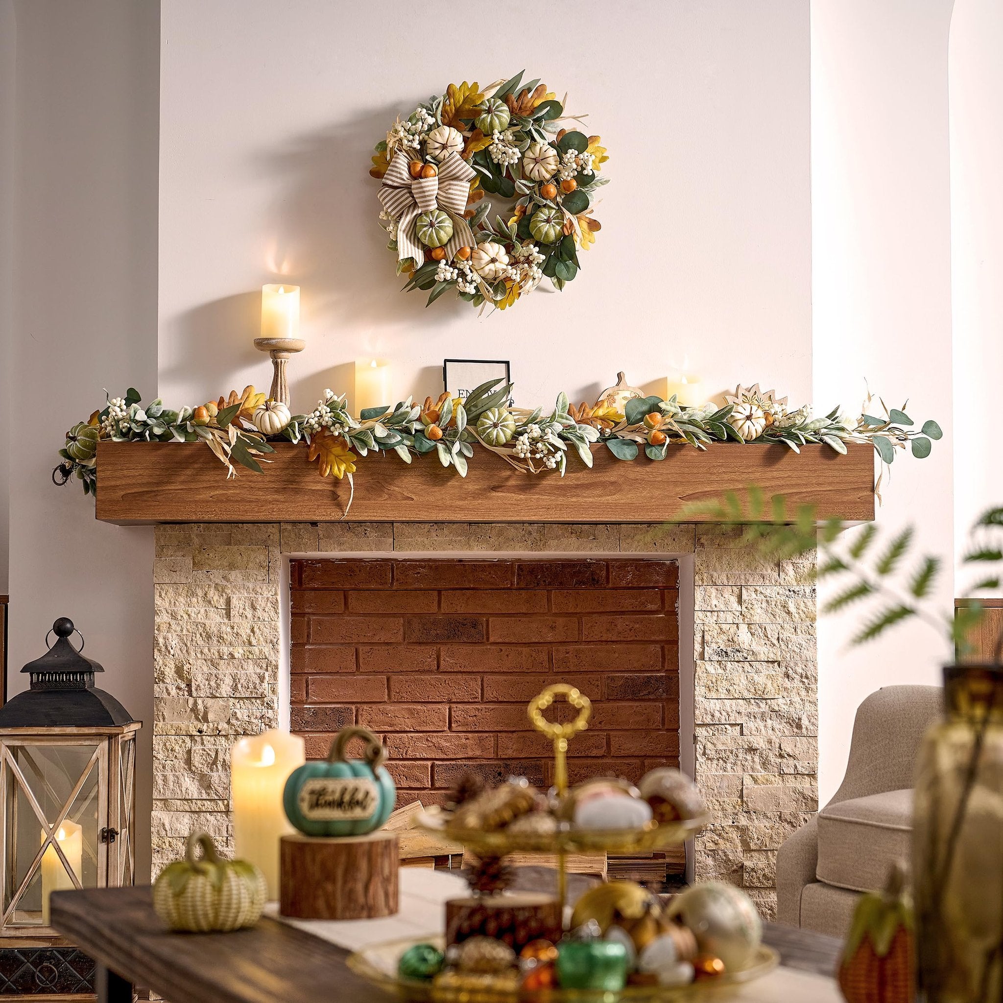 Fall wreath with pumpkins and burlap bow hangs above a garland on a fireplace mantel.