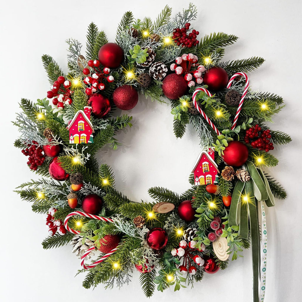 Festive Christmas wreath with pine branches, red ornaments, candy canes, pine cones, berries, and small house decorations, illuminated by warm LED lights.