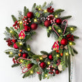 Festive Christmas wreath with pine branches, red ornaments, candy canes, pine cones, berries, and small house decorations, illuminated by warm LED lights.